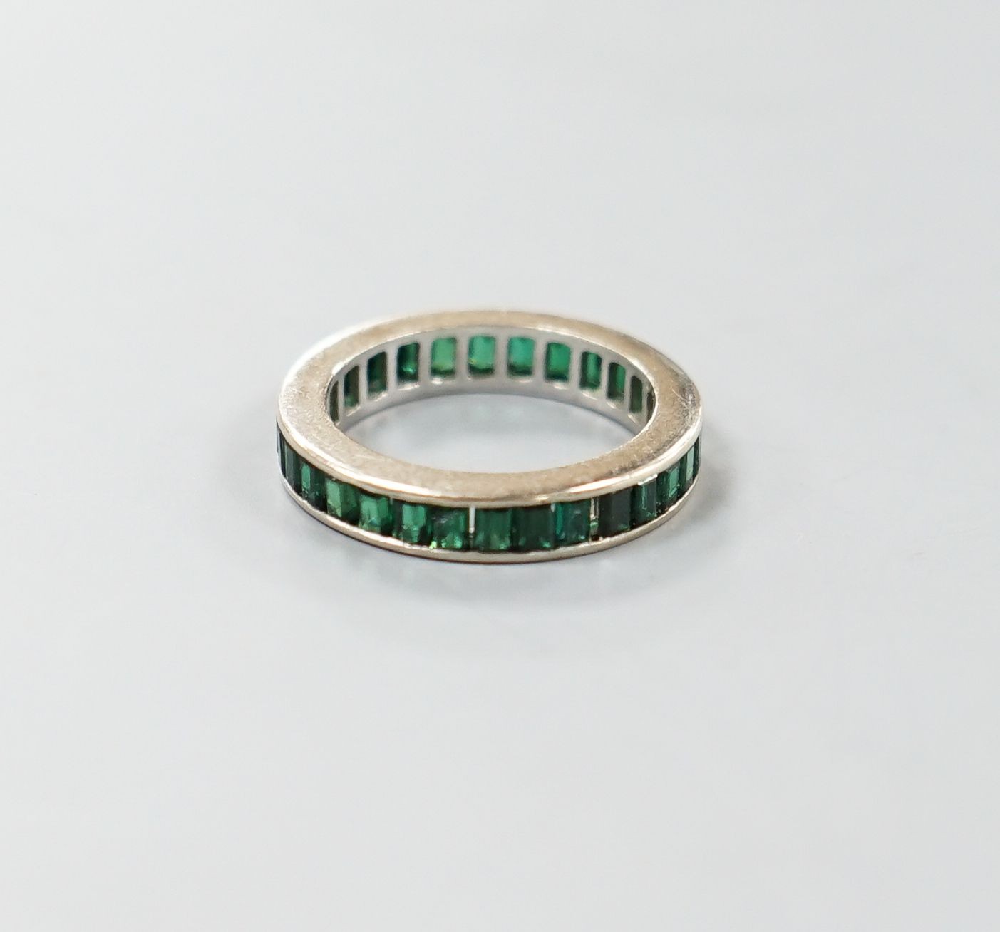 A white metal and green garnet? set full eternity ring, size L, gross weight 3.3 grams.